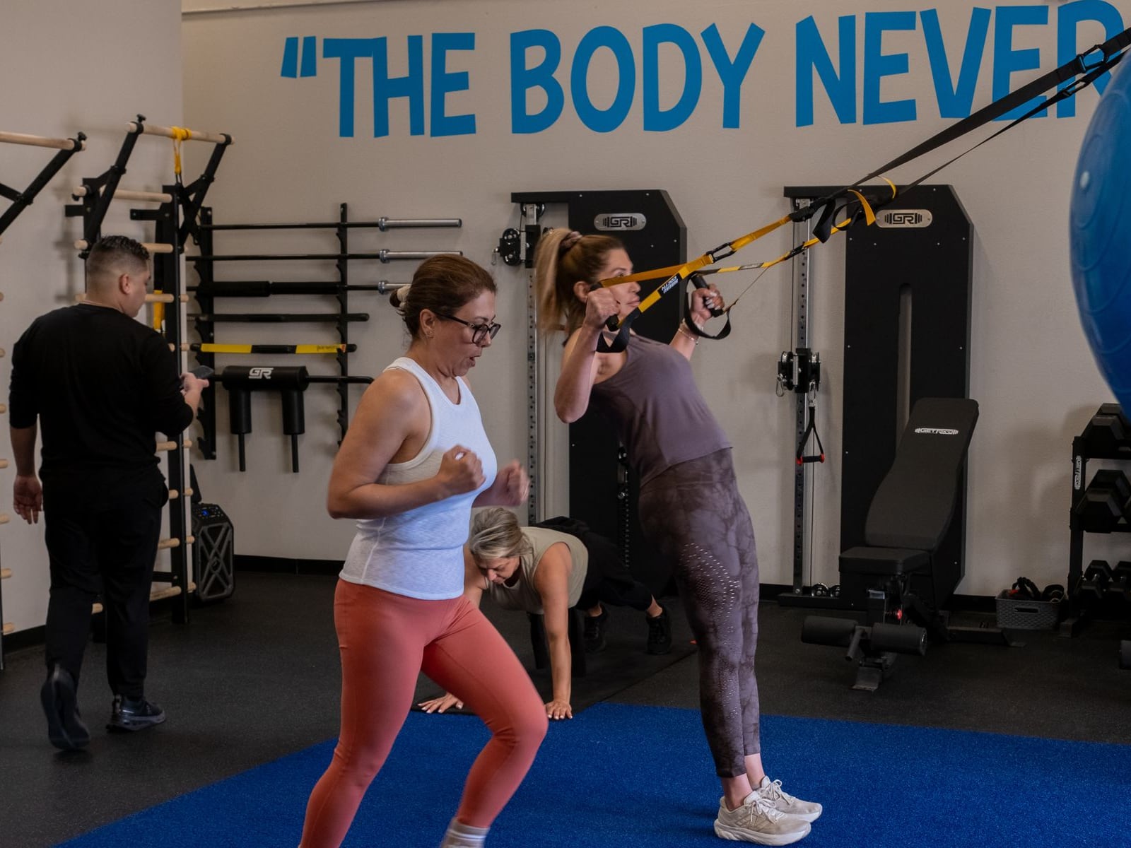 Three clients working through a semi-private session at IMTI, a coach nearby, under the painted wall that reads The Body Never Lies