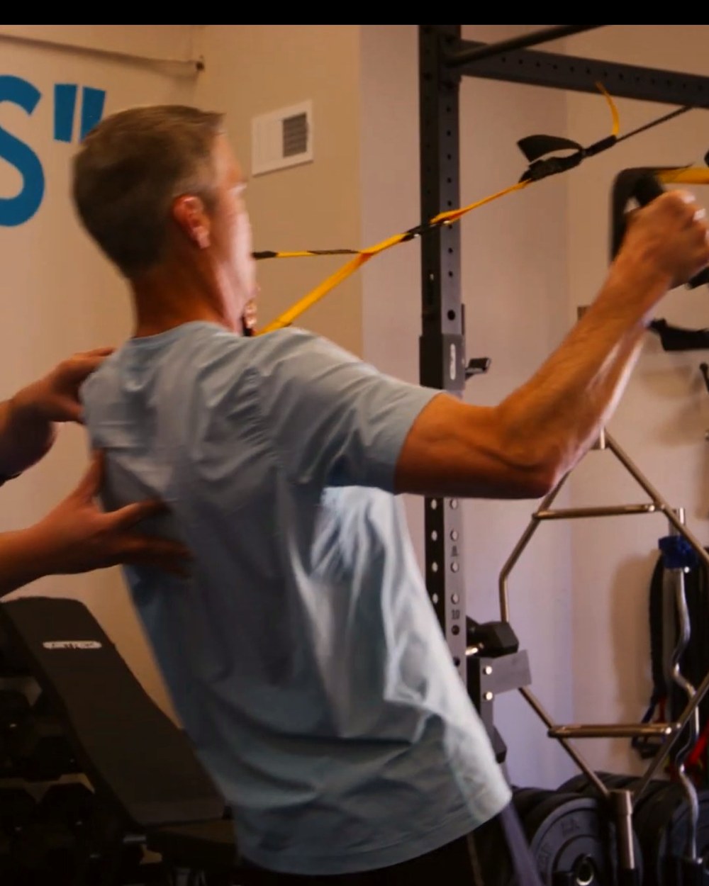 A coach’s hands squaring a client’s shoulders as he works the straps