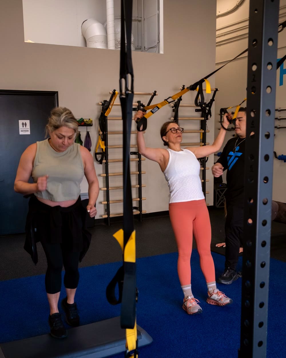 Two IMTI clients working through different exercises side by side at the same rack, a coach alongside